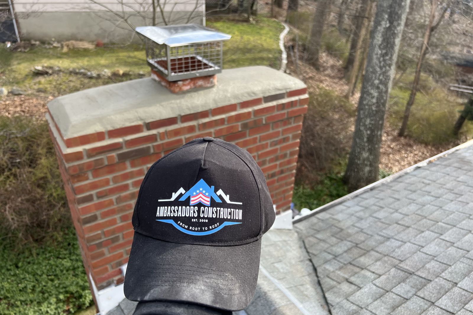 Ambassadors Construction branded cap in front of a repaired chimney on a New Jersey roof