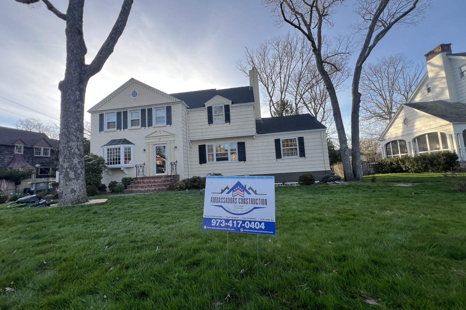 Completed roof replacement project on a New Jersey colonial home with Ambassadors Construction yard sign