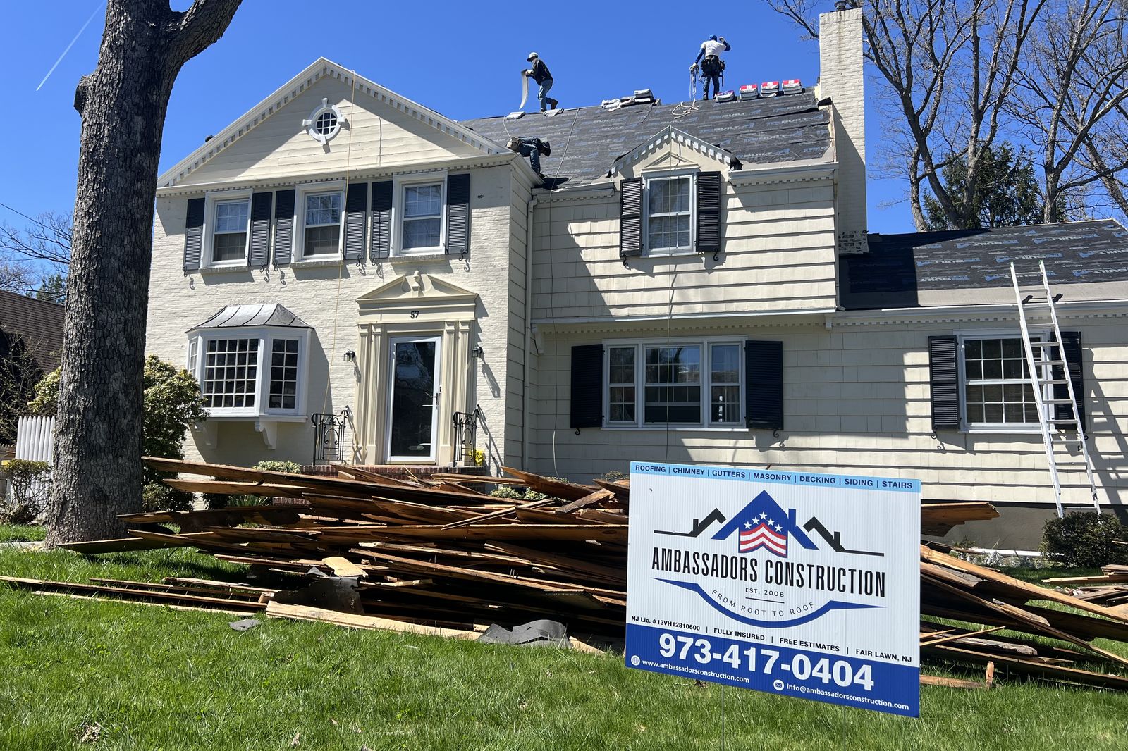 Ambassadors Construction yard sign in front of a New Jersey home during a roof replacement with crew on the roof