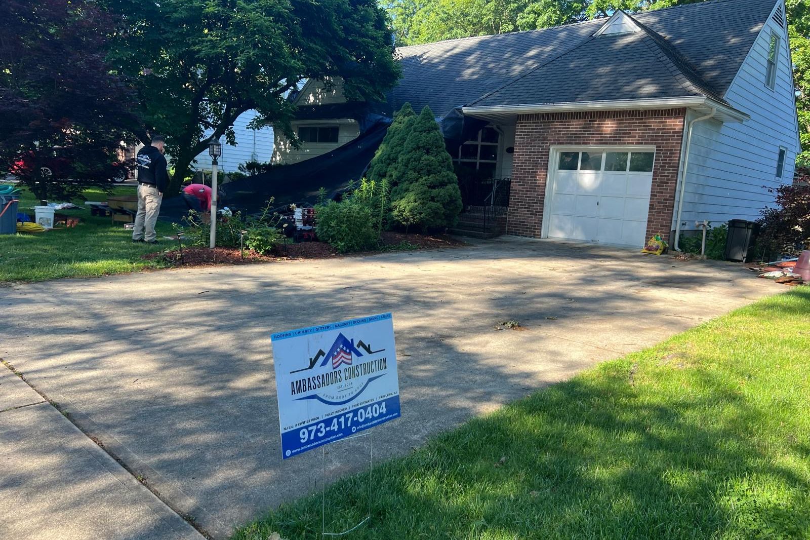 Ambassadors Construction yard sign in front of a New Jersey home with a tarped roof after storm damage